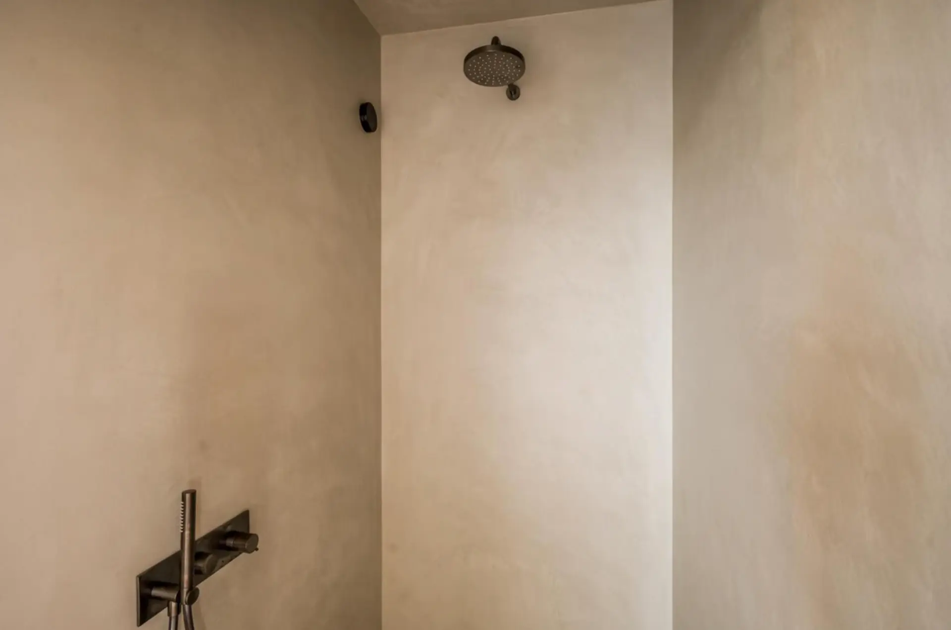 Shower enclosure in light sand-beige microcement with dark bronze fixtures