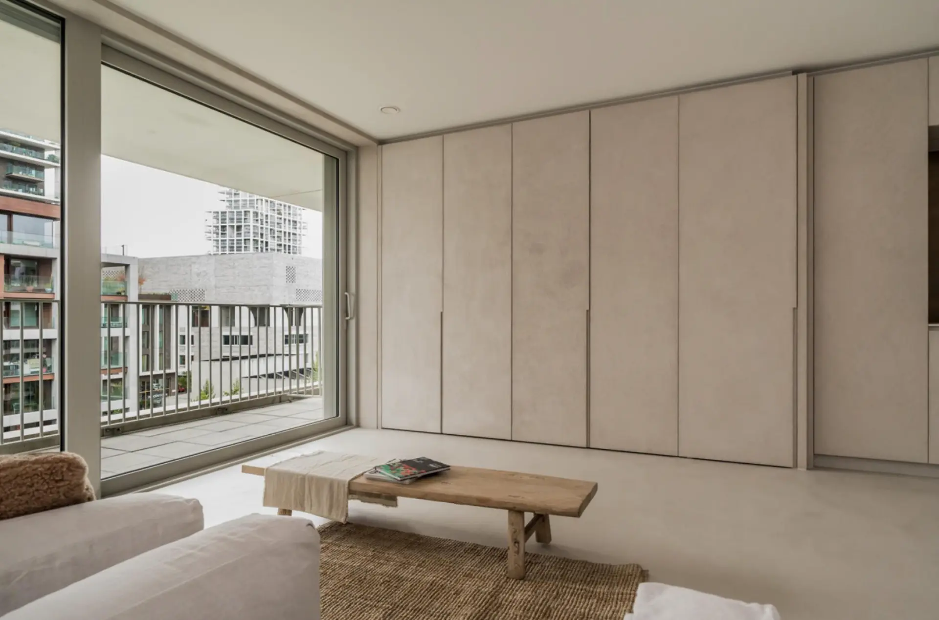Full-height built-in wardrobe panels and seamless flooring in warm greige microcement