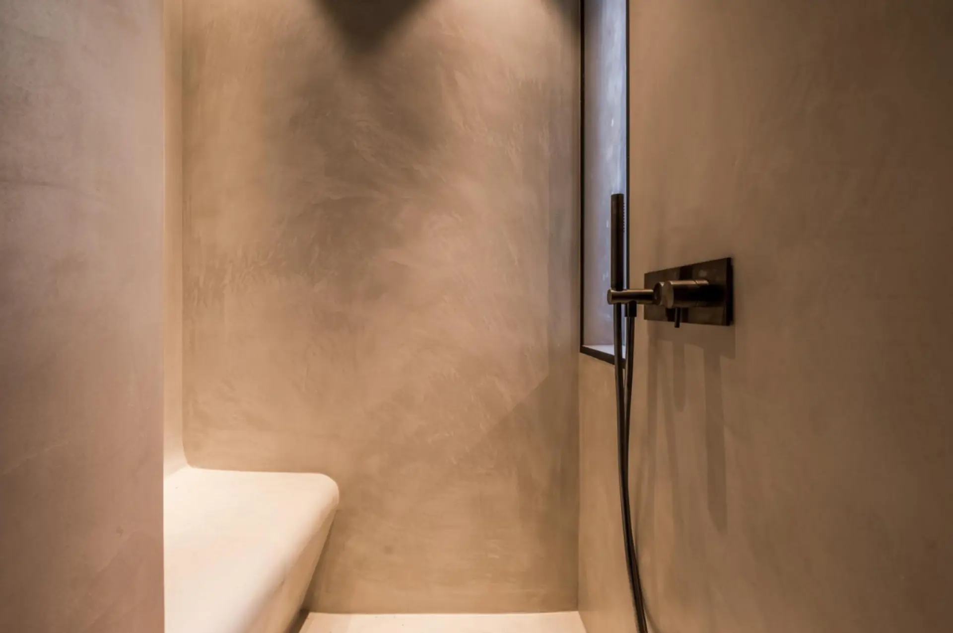 Walk-in shower in warm beige microcement with a built-in bench