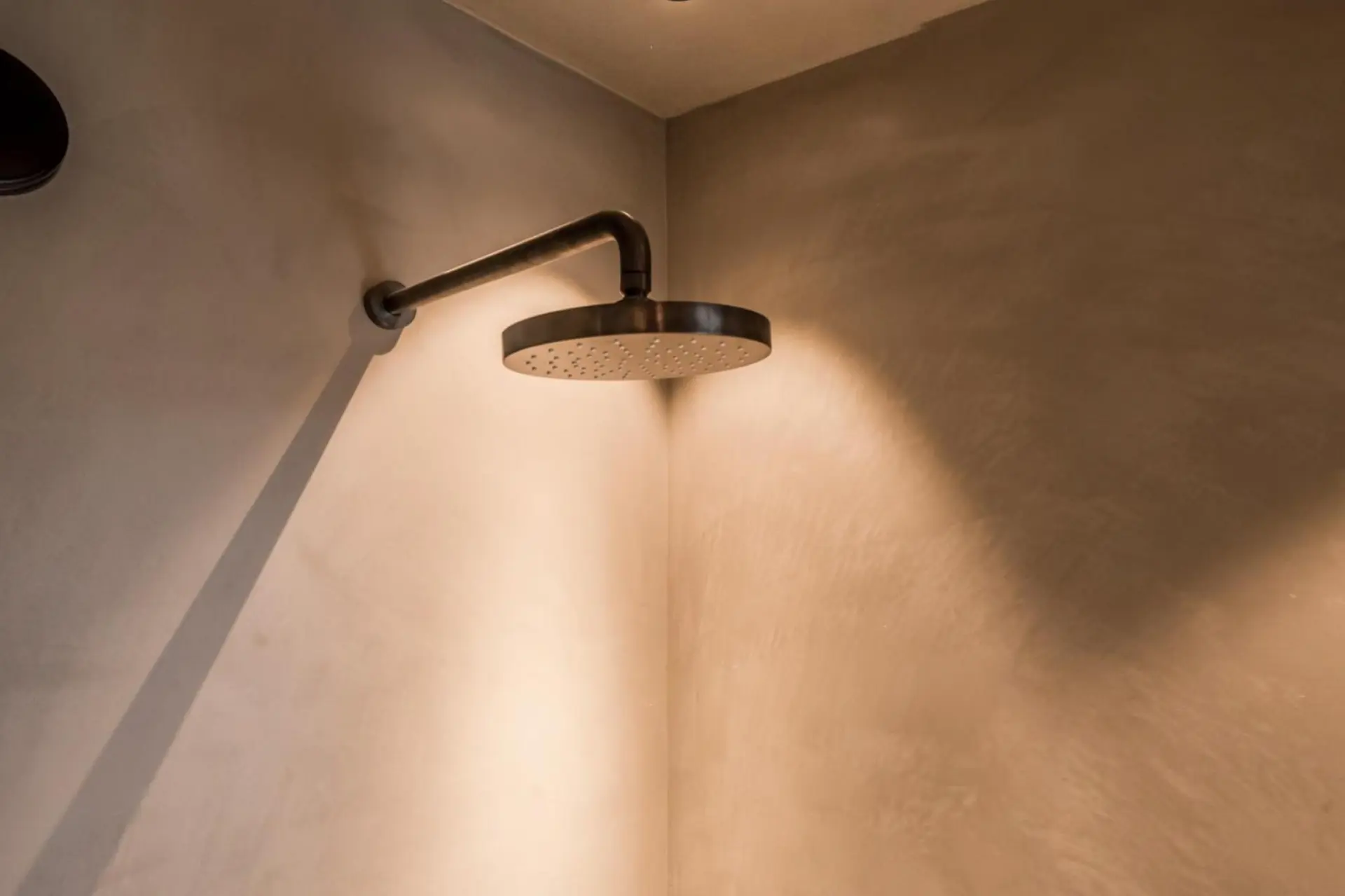 Shower corner in warm taupe microcement with a dark metal rain shower head