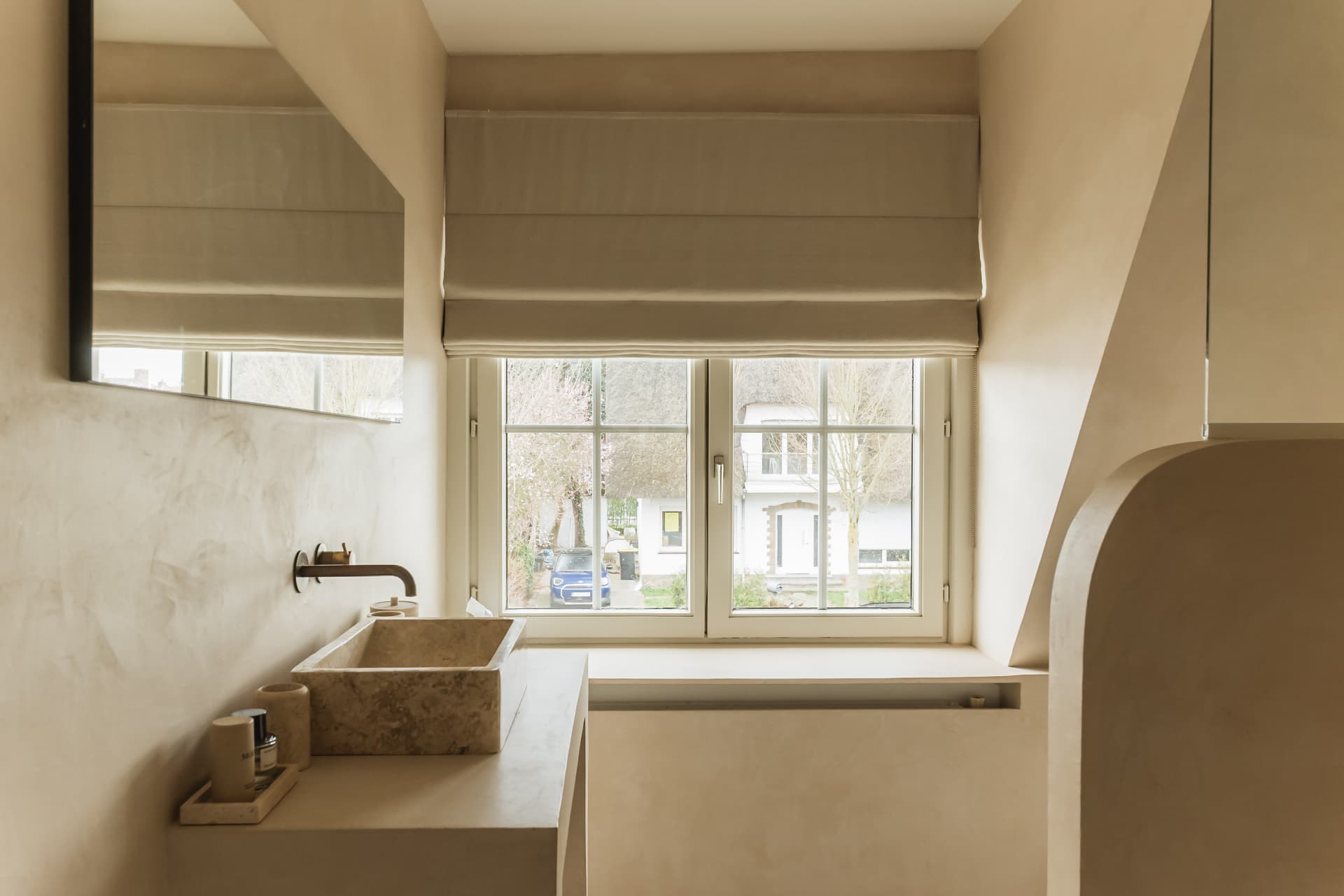 Bathroom vanity with a carved stone vessel sink on a plaster counter beneath a cottage window