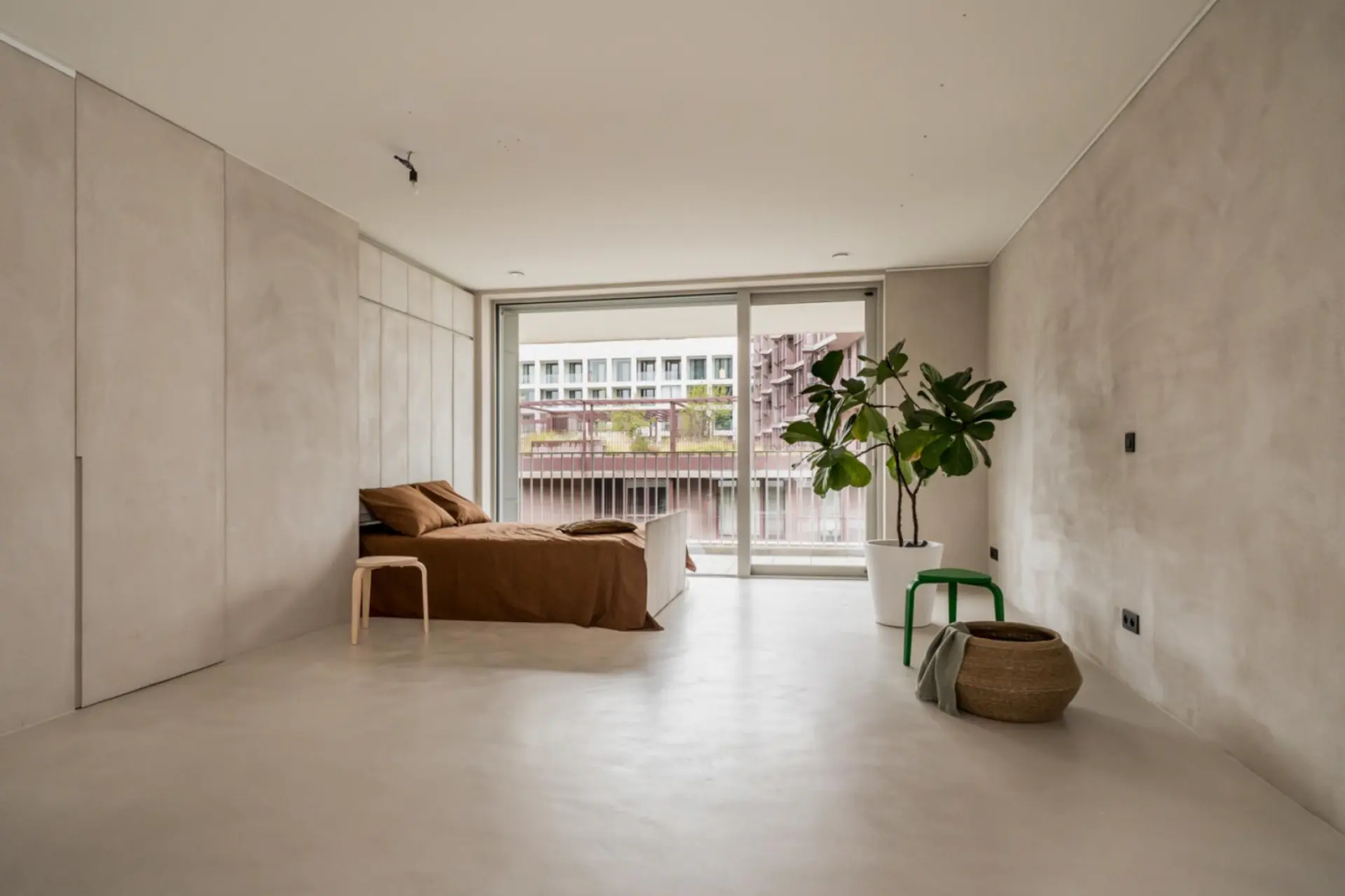 Bedroom with light greige microcement floors and walls beneath daylight from sliding balcony doors